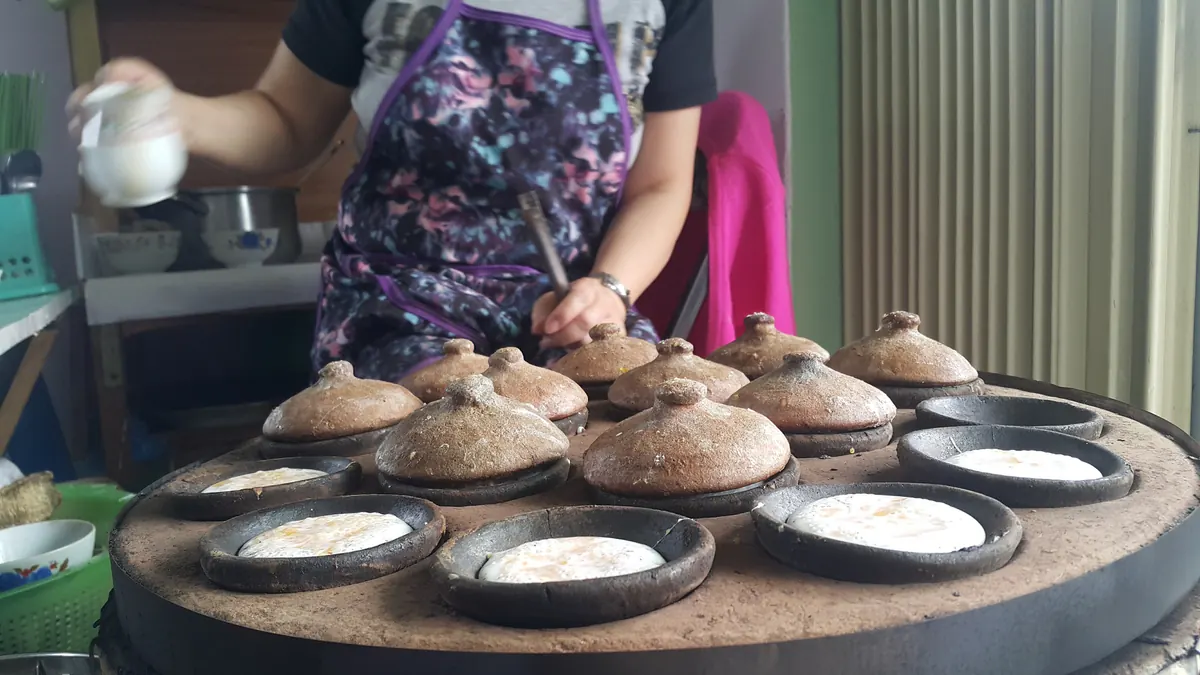 Người bán đổ bột bánh căn vào dãy khuôn đất nung có nắp đậy