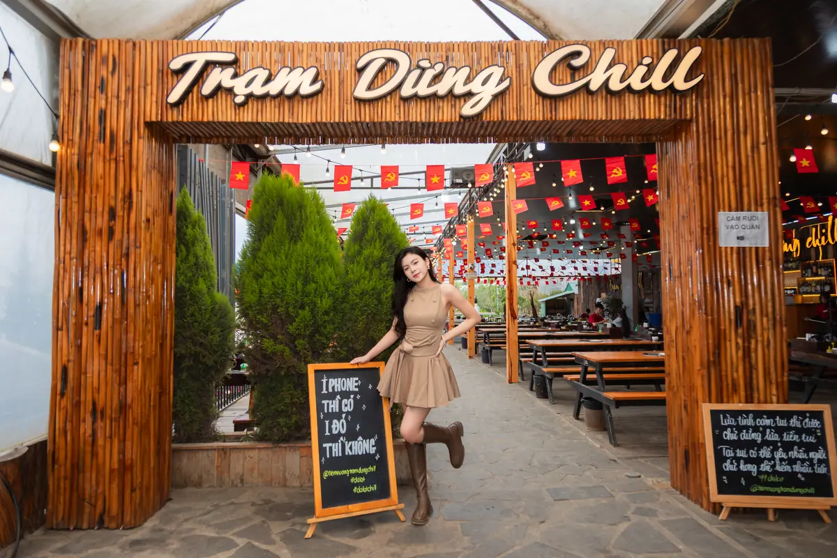 Khách tạo dáng ở cổng tre gắn biển Trạm Dừng Chill, bên trong là dãy bàn gỗ và cờ đỏ